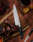 Chef's knife on a wooden cutting board with cooked meat, spices, and a bowl of sauce.