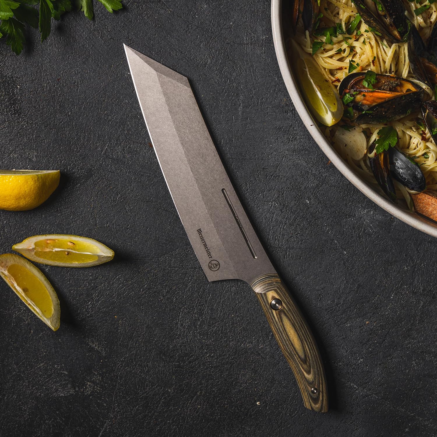 Chef's knife on a dark surface with lemons and a dish of pasta with mussels.