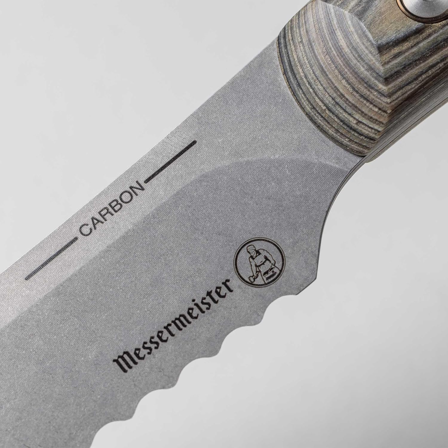 Close-up of a Messermeister knife blade with 'Carbon' and brand logo on a light gray background