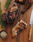 Sliced grilled chicken on a wooden cutting board with rosemary and a knife.