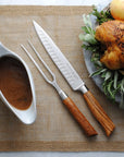 Roasted chicken with carving utensils and a gravy boat on a woven mat