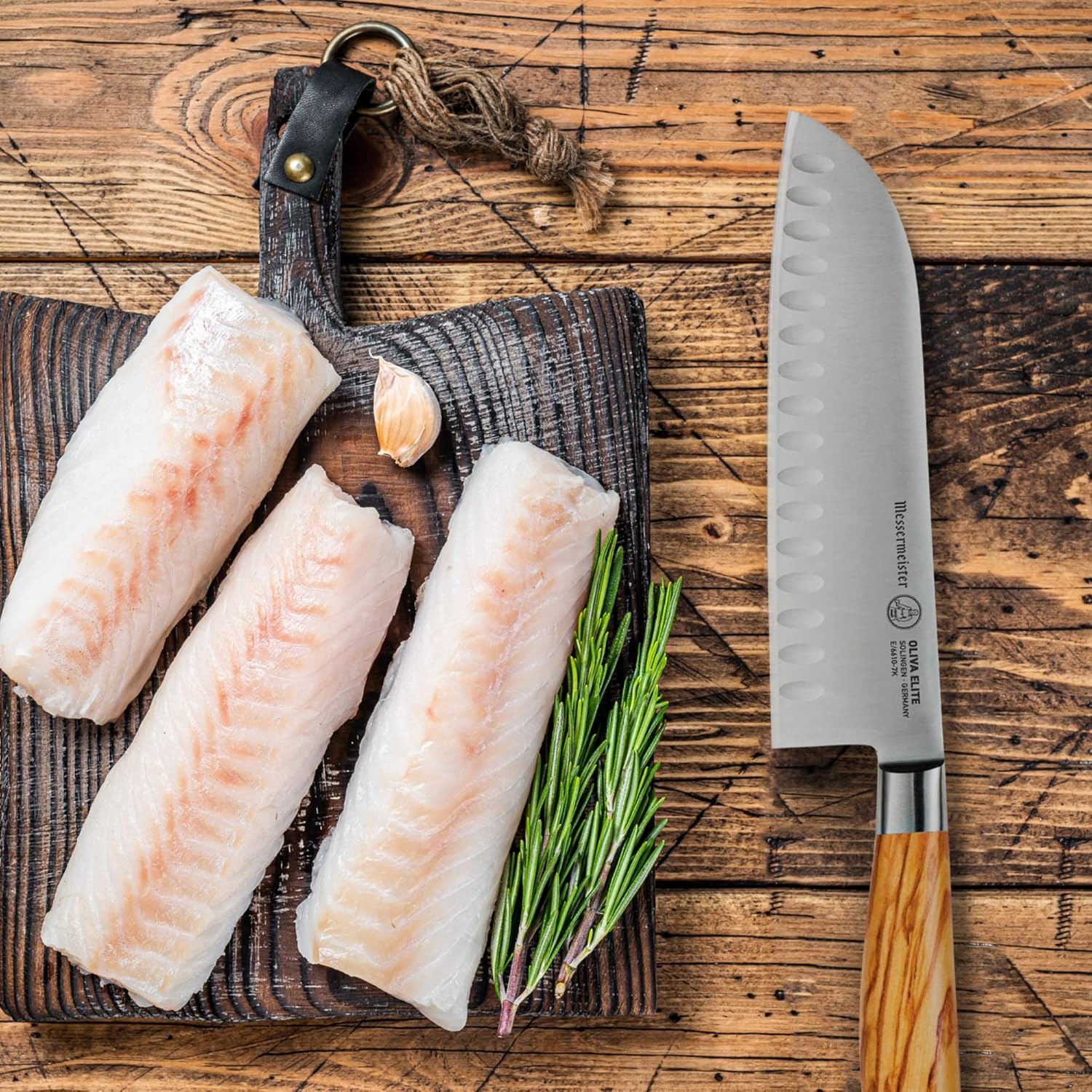 Three raw fish fillets on a wooden board with a knife next to them.