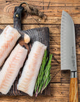 Three raw fish fillets on a wooden board with a knife next to them.