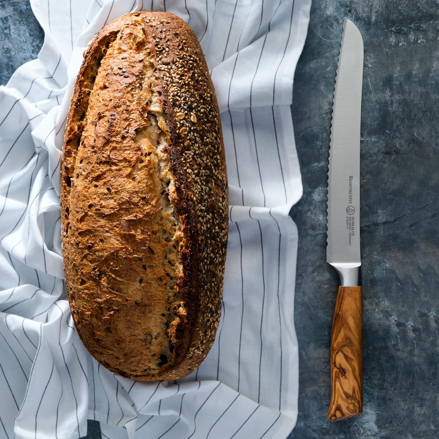 Loaf of bread with a knife on a striped cloth and gray surface
