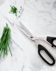 Scissors with black handles on a marble surface next to chopped green herbs
