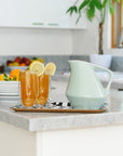 Two glasses of iced tea with lemon slices on a kitchen counter, accompanied by a sage green pitcher.