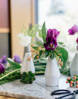 Decorative setting with white vases, purple tulips, and greenery on a marble surface.
