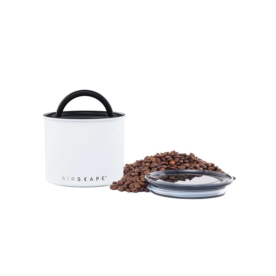 White coffee canister with black lid and handle, surrounded by coffee beans on a white background.
