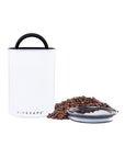 White air-tight container with black handle and lid, filled with coffee beans on a white background.