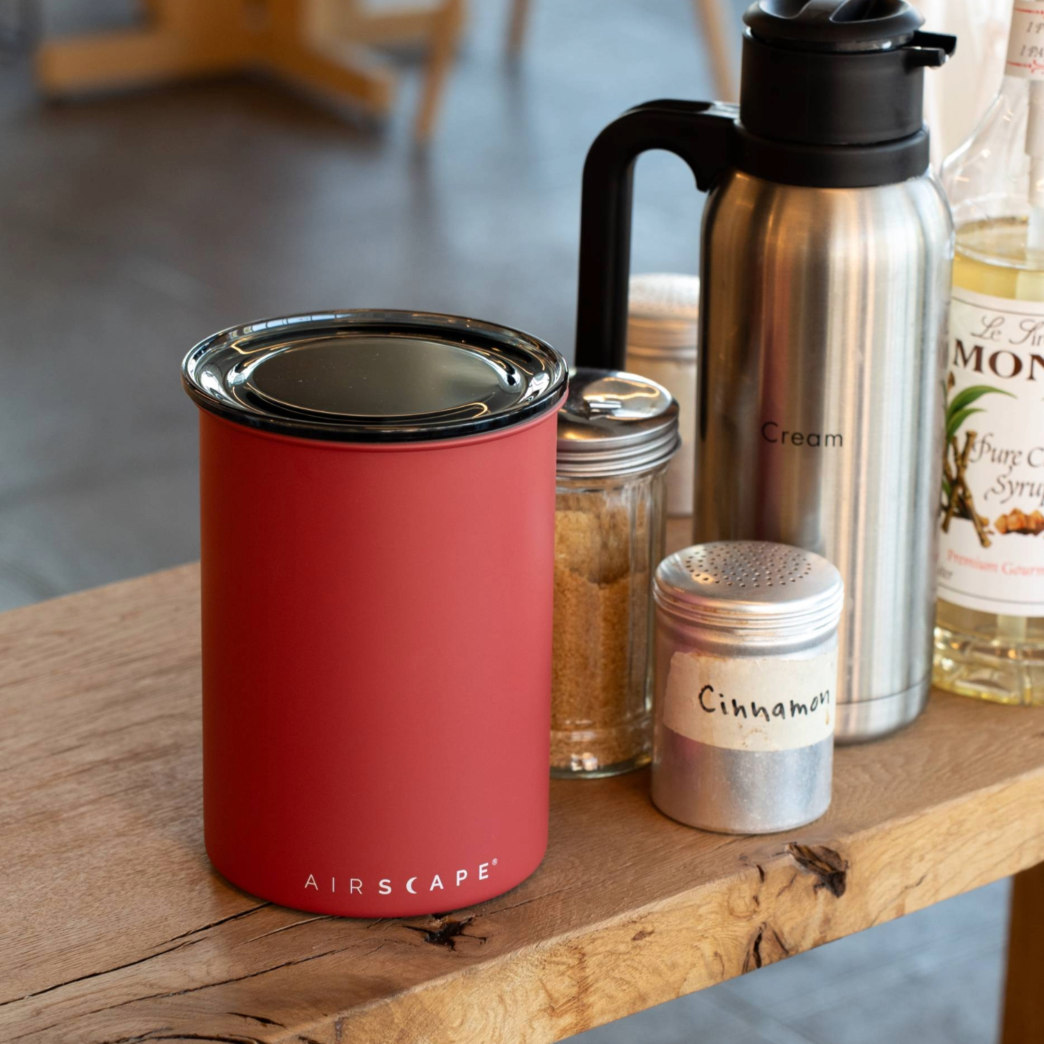 Red container, silver thermos, and spice jars on a wooden surface with a blurred background.