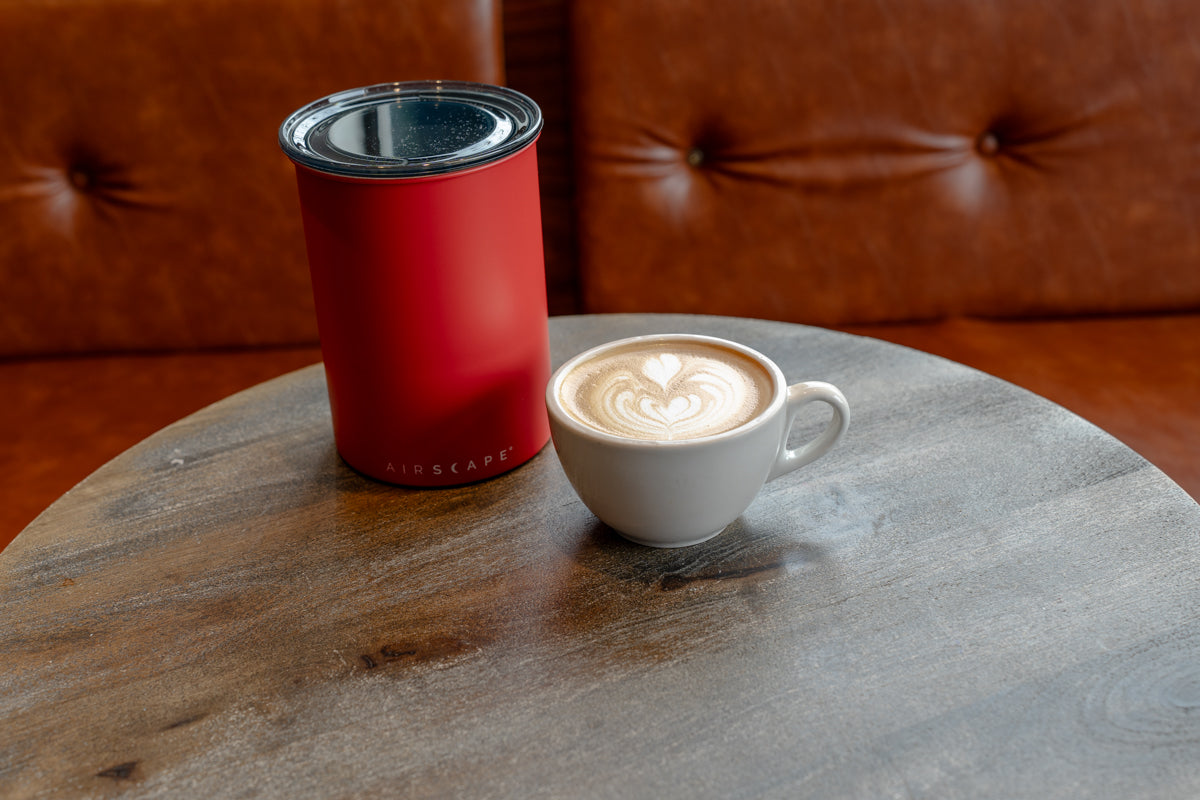 Red insulated container and white mug with latte on a wooden table