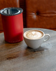 Red insulated container and white mug with latte on a wooden table