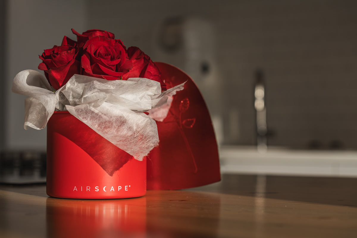 Red floral arrangement in an 'AIRSCAPE' container on a wooden surface with a blurred background.