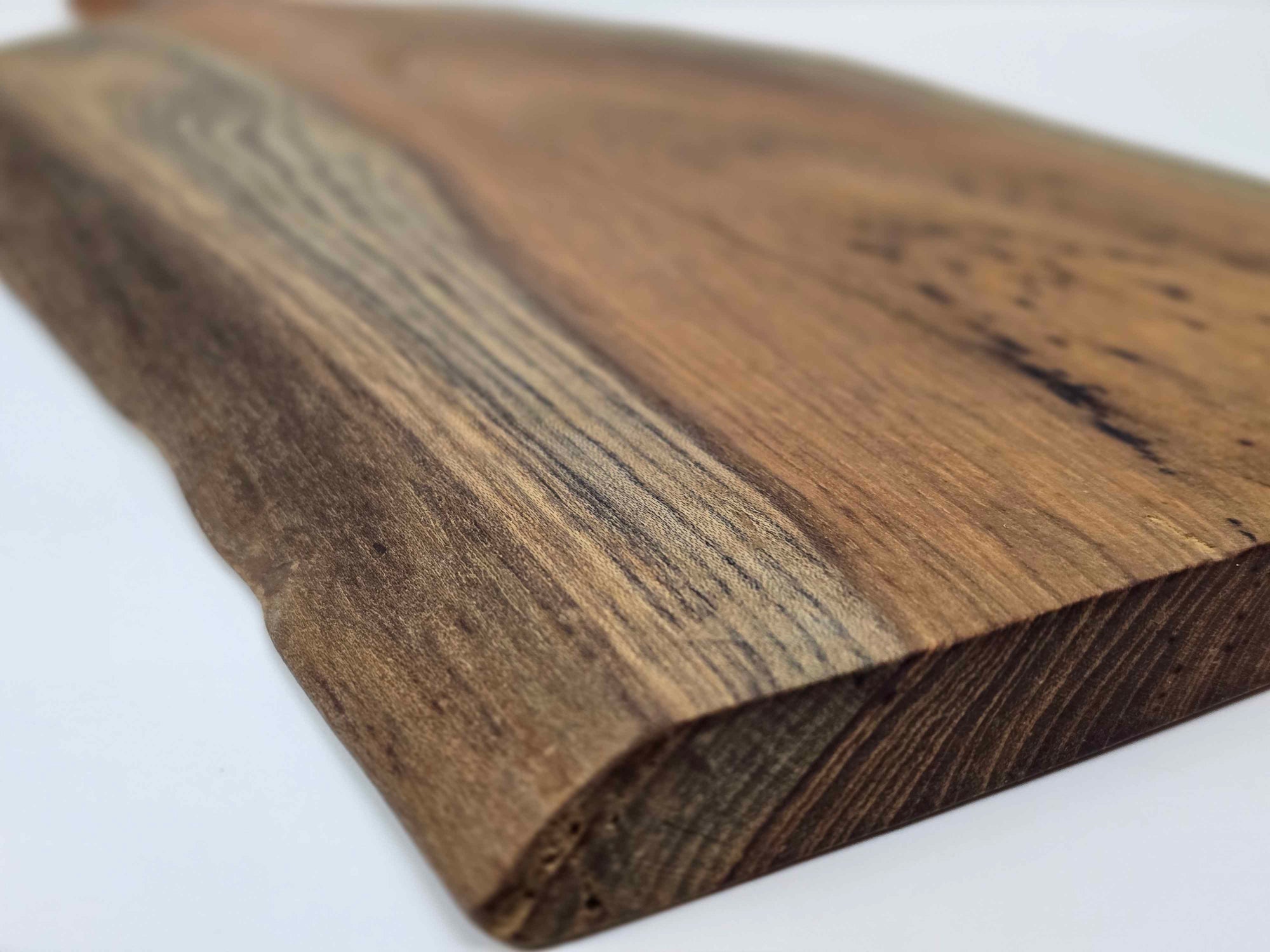 Close-up of a wooden cutting board showing the natural edge with a white background