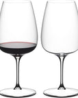 Two wine glasses, one filled with red wine, on a white background