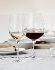 Two clear wine glasses on a table, one filled with white wine and one with red wine, alongside a clear drinking glass in a softly lit dining setting.
