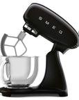 Black Smeg stand mixer slanted open with clear mixing bowl on a white background