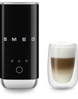 Black SMEG milk frother next to a glass of creamy coffee on a white background