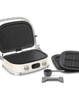 Cream Smeg grill with silver accents with an assortment of attachments on a white background