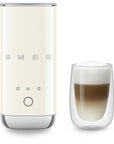 Cream SMEG milk frother next to a glass of creamy coffee on a white background