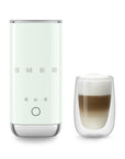 Pastel green SMEG milk frother next to a glass of creamy coffee on a white background