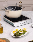 Induction cooktop with a pot on a kitchen counter, featuring a plate of eggs and asparagus.