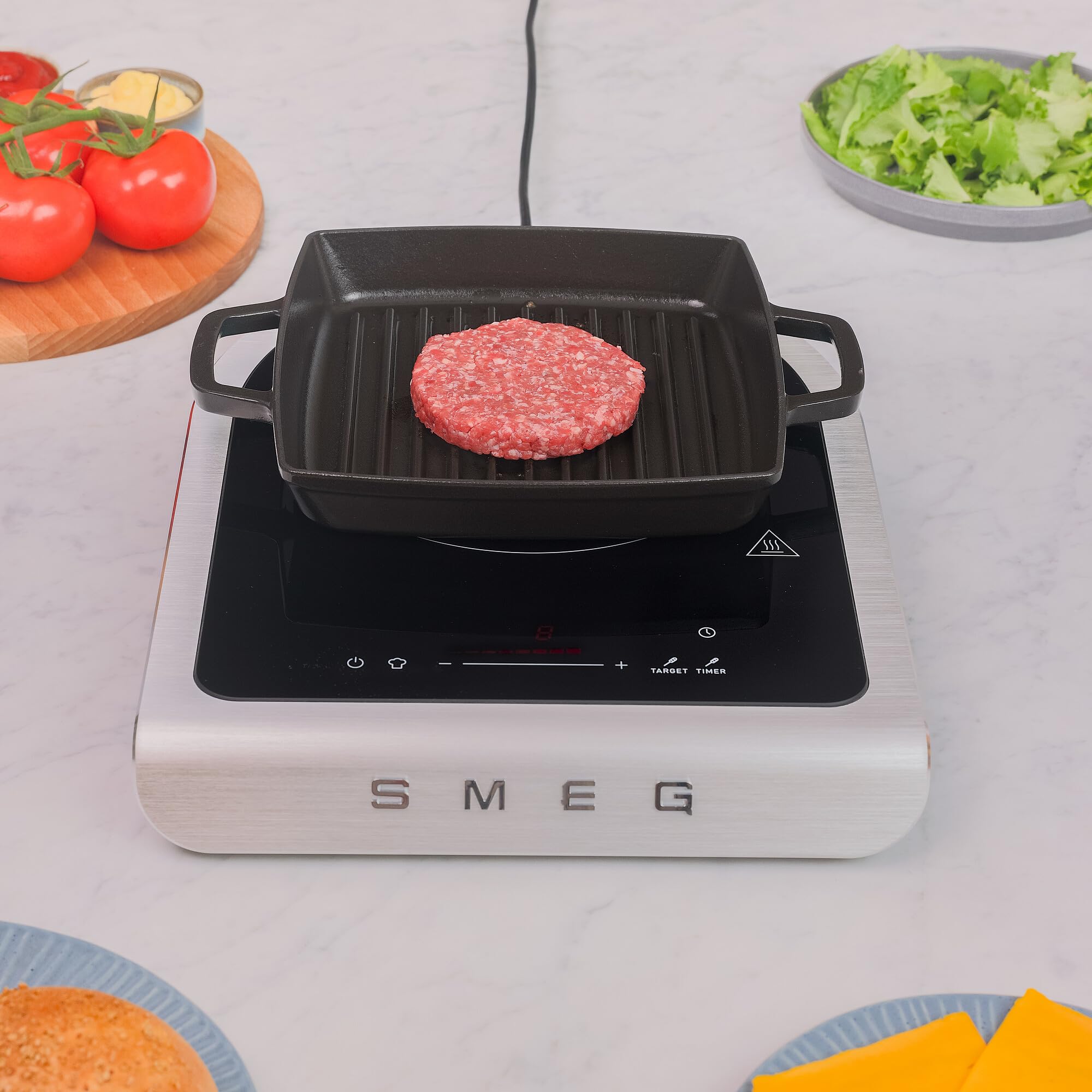 SMEG induction cooktop with a grill pan on a kitchen counter with ingredients.