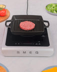 SMEG induction cooktop with a grill pan on a kitchen counter with ingredients.