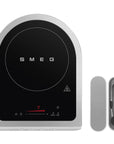SMEG induction cooktop with control panel and accessories on a white background