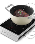Induction cooktop with a pot of beef being cooked and showing the temperature probe being used on a white background
