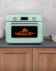 Pastel green Smeg retro line countertop air fry oven on a kitchen counter with food inside, surrounded by kitchen items.