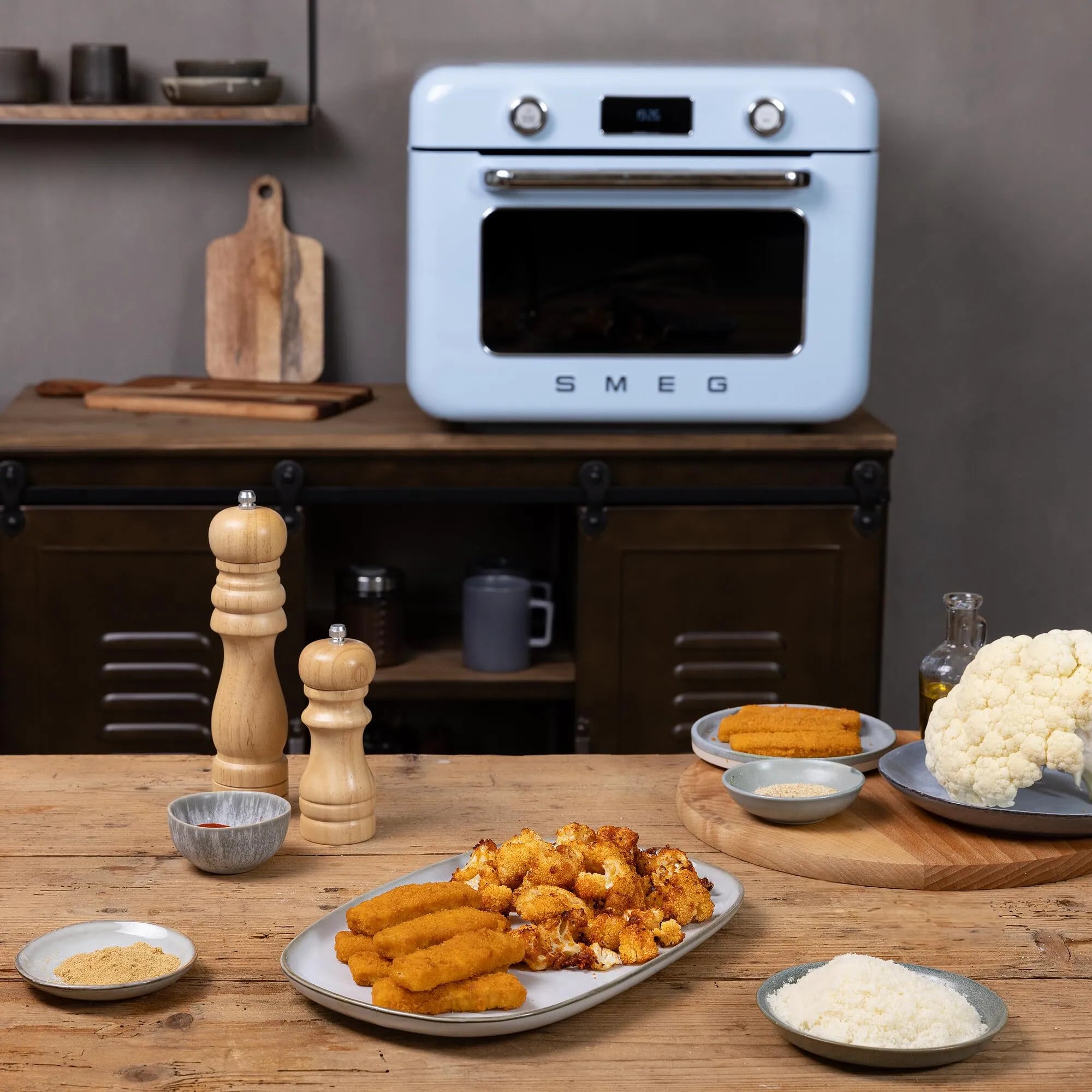 Kitchen scene with a pastel blue Smeg oven, wooden table, and plates of food.