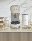 White Smeg coffee machine on a kitchen counter with various coffee items.