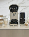Black Smeg coffee machine on a kitchen counter with various coffee items.