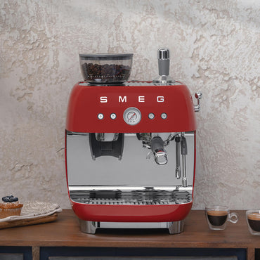 Red Smeg retro line espresso machine with coffee beans, espresso shots, and muffin on the side on a counter