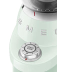 Close-up of a light green coffee grinder with 'Smeg' branding and dial on a white background