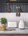 White toaster and kettle on a kitchen counter with a plant and bread loaf.
