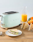 Mint green toaster on a wooden table with orange juice, toast, and fruit.
