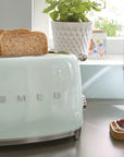 Vintage-style mint green toaster with two slices of toast, placed on a kitchen counter.