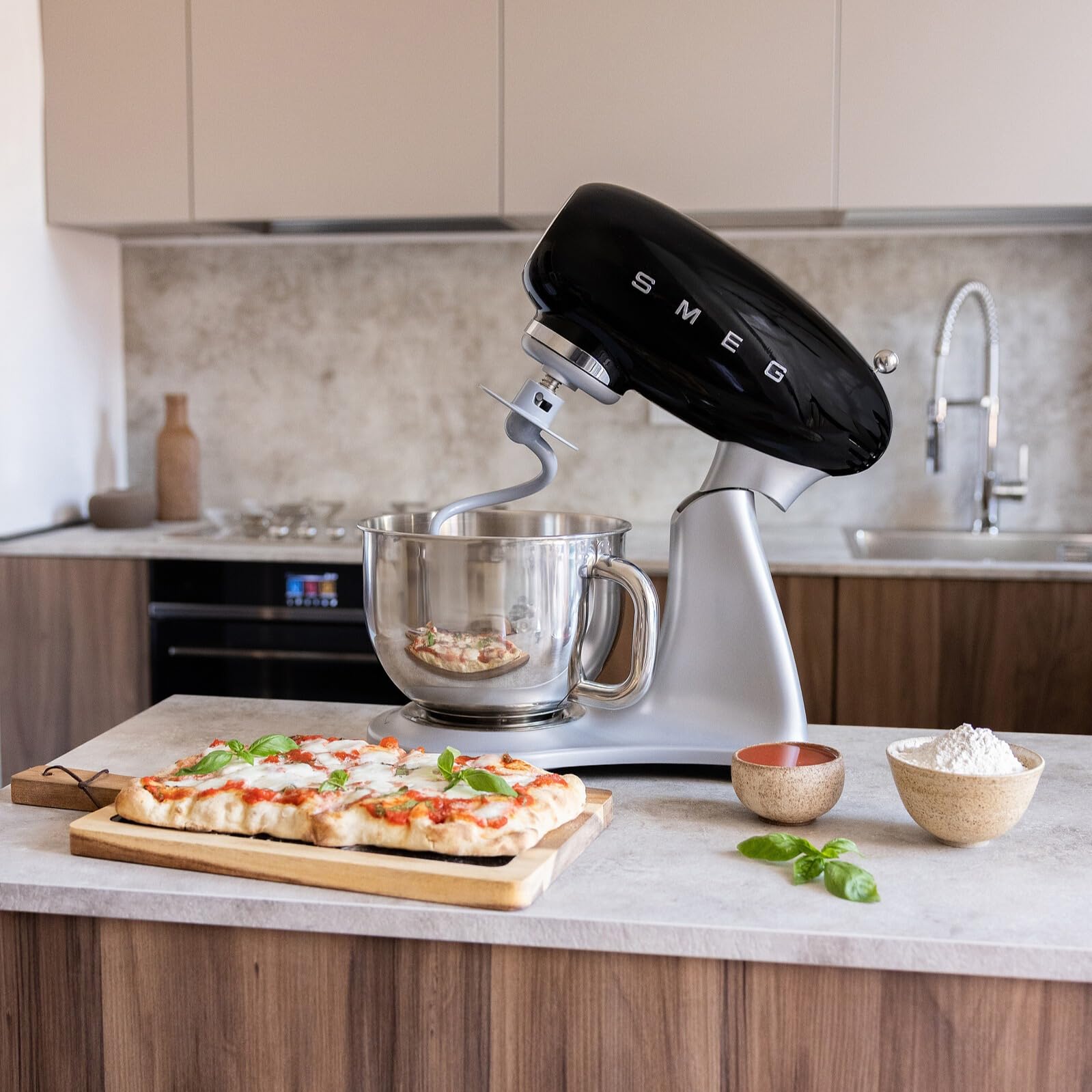 Black Smeg stand mixer on a kitchen counter with a pizza and ingredients