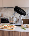 Black Smeg stand mixer on a kitchen counter with a pizza and ingredients