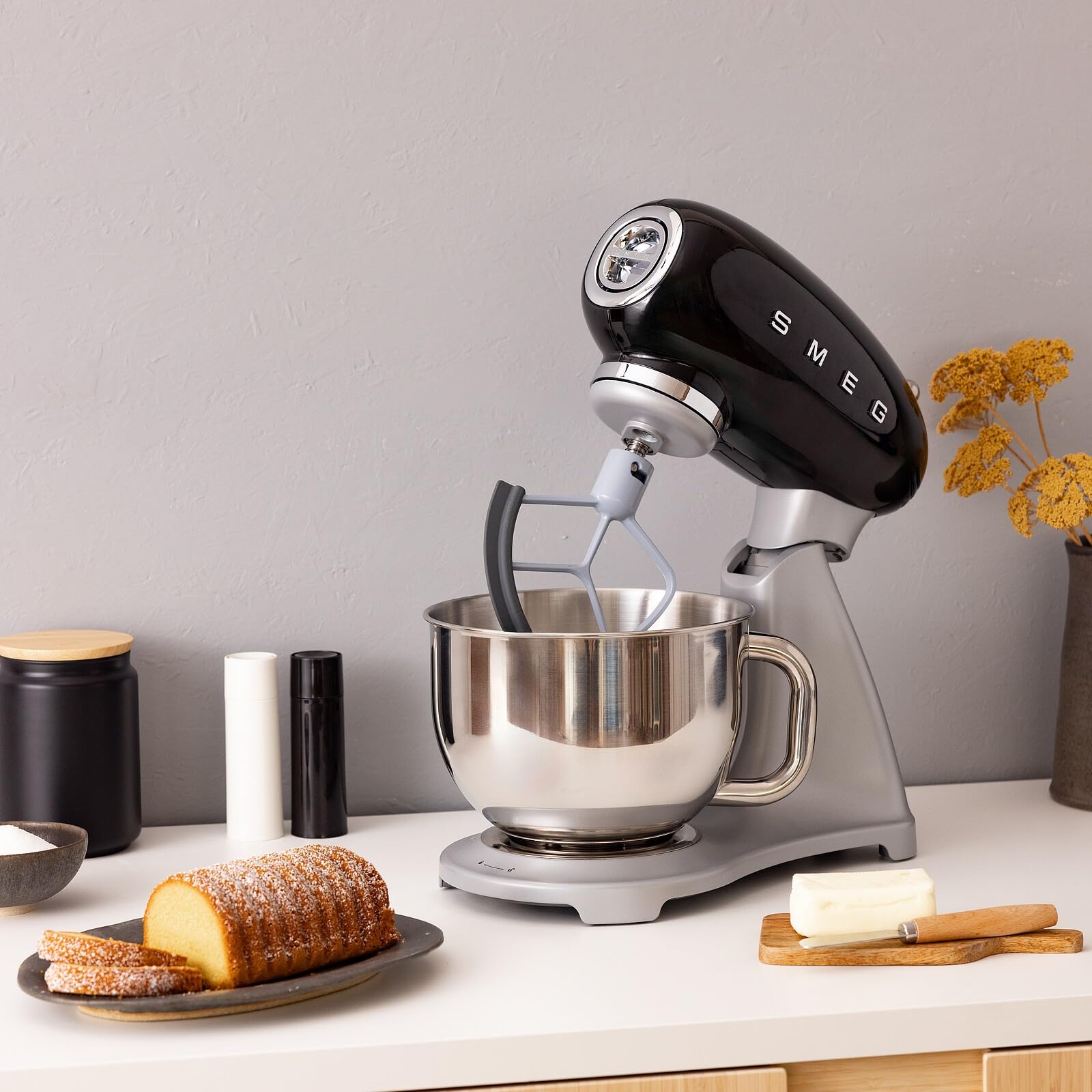Black SMEG stand mixer on a kitchen counter with baked goods and utensils.
