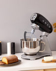 Black SMEG stand mixer on a kitchen counter with baked goods and utensils.