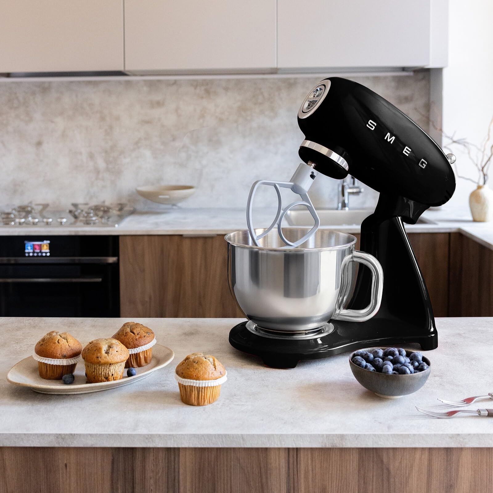 Black Smeg stand mixer on a kitchen counter with muffins and blueberries.