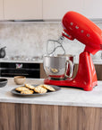 Red Smeg stand mixer on a kitchen counter with cookies and bowls.