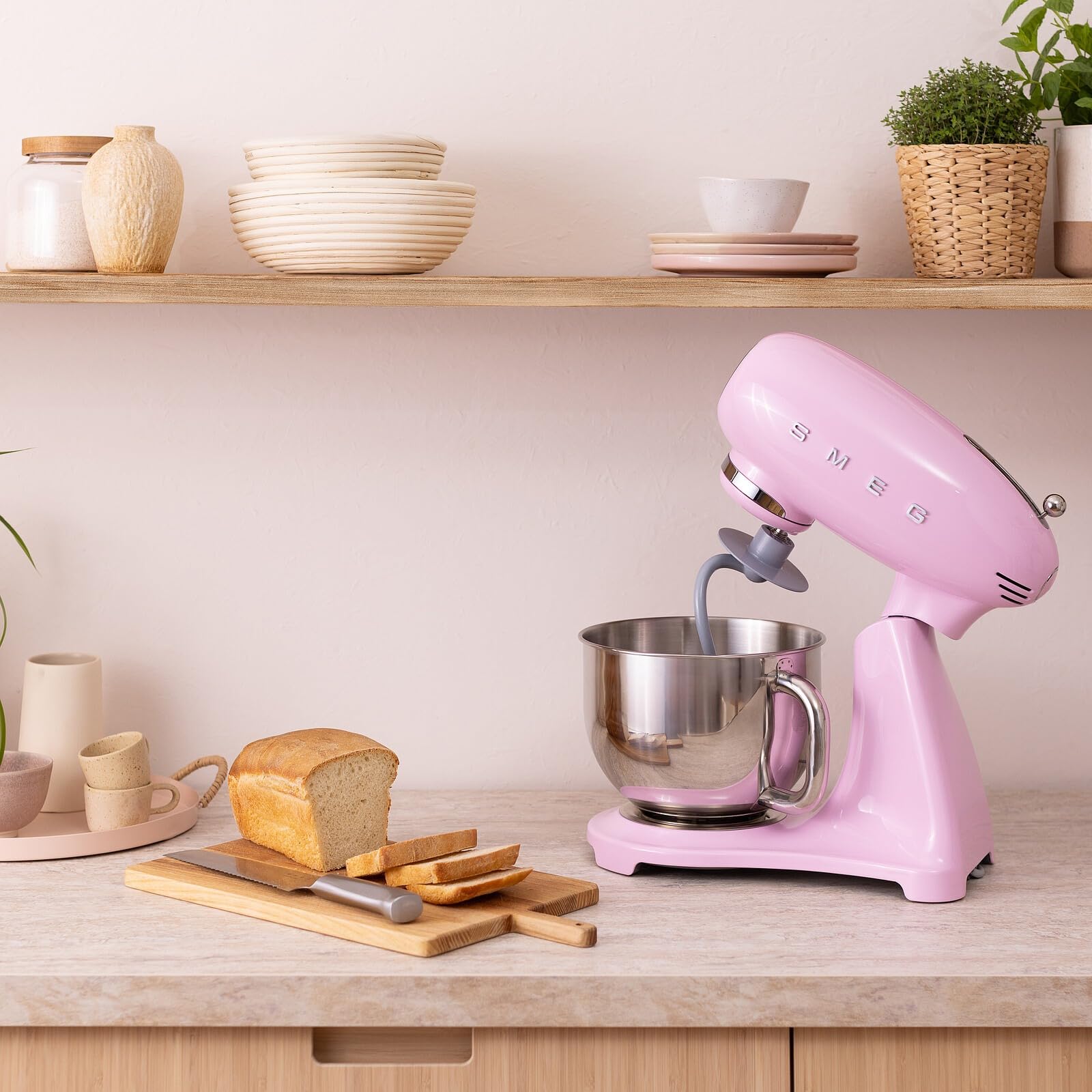 Pink stand mixer on a kitchen counter with bread and utensils