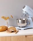Light blue Smeg stand mixer with a loaf of bread on a wooden board placed on  a countertop.