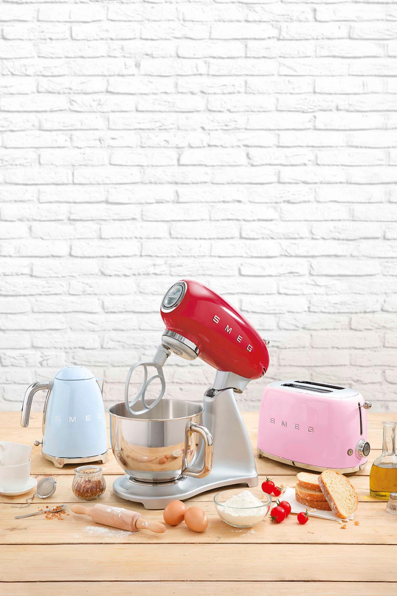 Red SMEG 50s Retro Line Full Color Stand Mixer 5 qt by a SMEG kettle and toaster next to cooking materials on a wooden surface