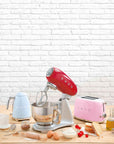 Red SMEG 50s Retro Line Full Color Stand Mixer 5 qt by a SMEG kettle and toaster next to cooking materials on a wooden surface