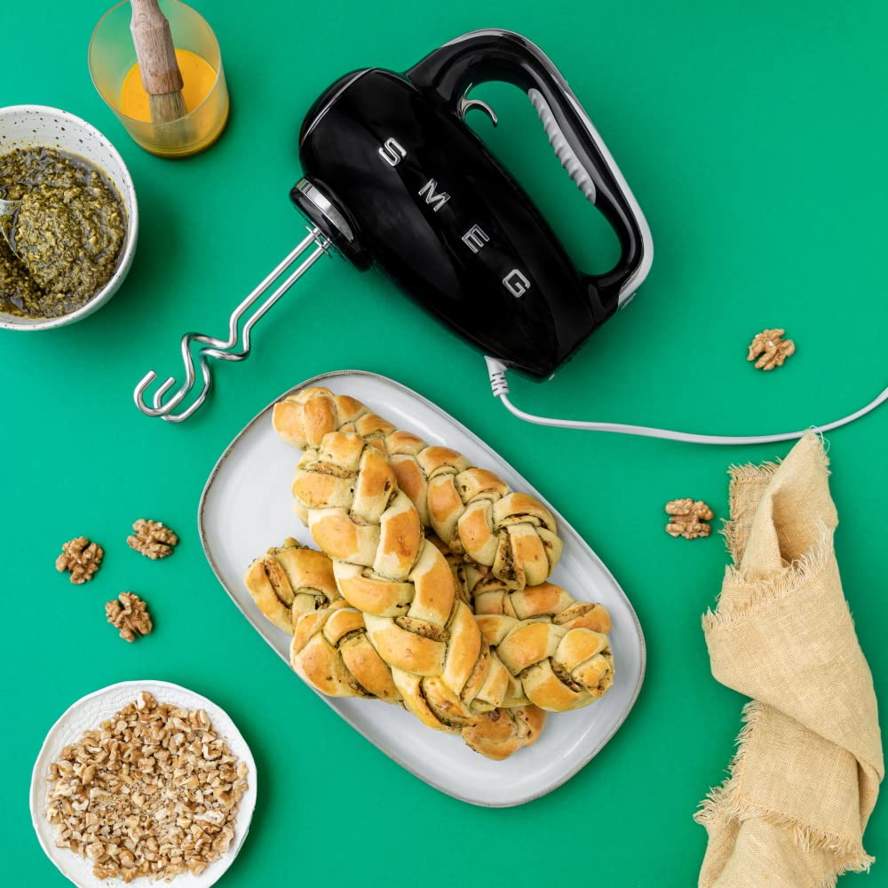Black Smeg hand mixer on a green background with bread and ingredients